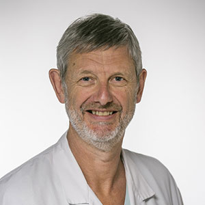 A man in a white doctor's coat smiles in front of a white back drop.