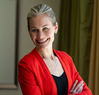 safeheal-jenny-gaffney-2025 A blonde professional in a red blazer smiles in front of a corporate office background